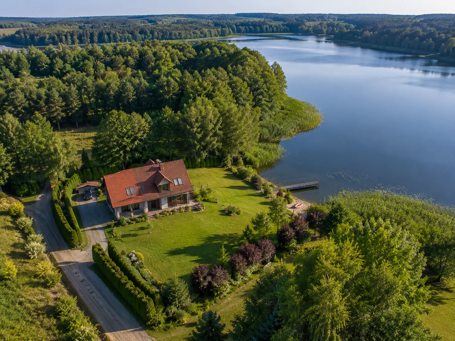 Dom nad jeziorem pokazany z drona z widoczną działką, linią brzegową, dojściem do wody i prywatnym pomostem